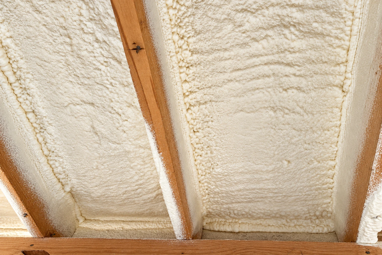 White spray foam seals the underside of a roof between exposed wooden rafters.