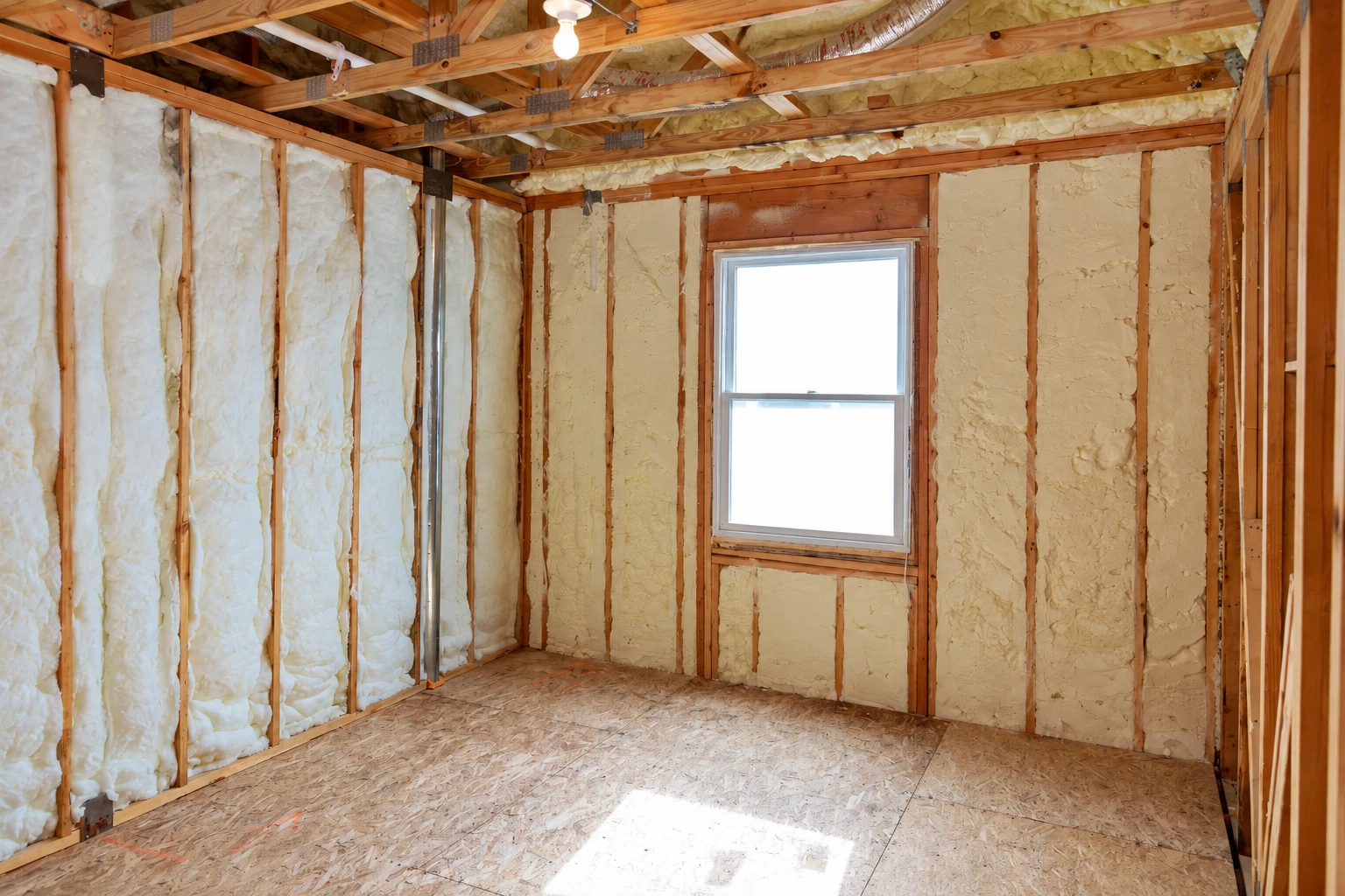 Unfinished room with pale insulation fitted between wall studs around a central window.